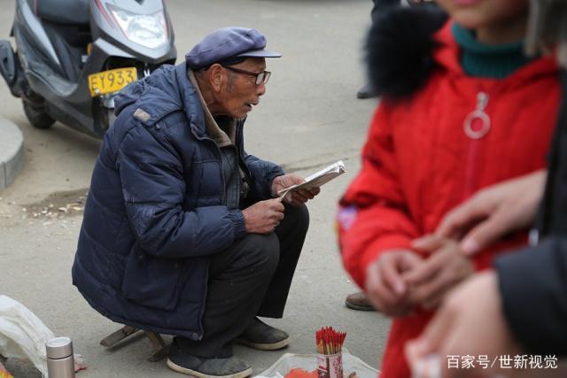 节上,一位长者戴着老花眼镜,手里拿着一本卦书,正在帮一位老奶奶算命